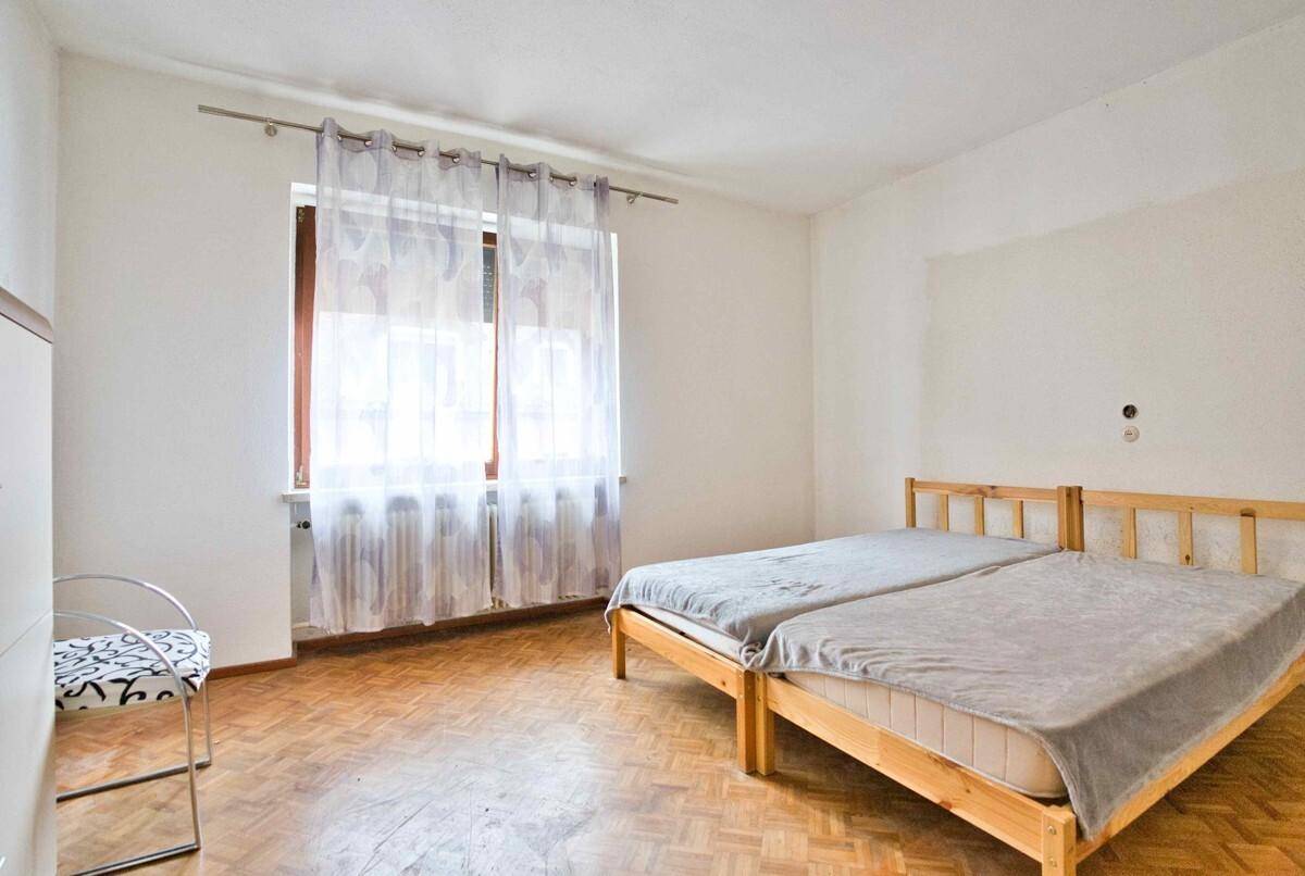 Schlafzimmer mit zwei Einzelbetten und hellem Parkettboden, gut beleuchtet durch ein Fenster.