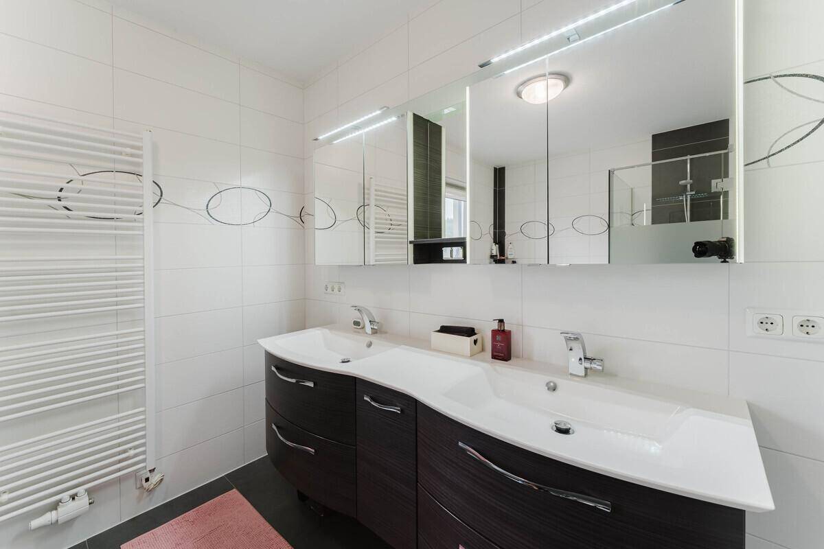 Helles Badezimmer mit Doppelwaschbecken, großem Spiegelschrank und Handtuchheizkörper.
