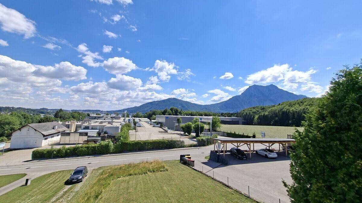 Weitläufiger Blick über ein Gewerbegebiet mit Bergen im Hintergrund unter blauem Himmel.