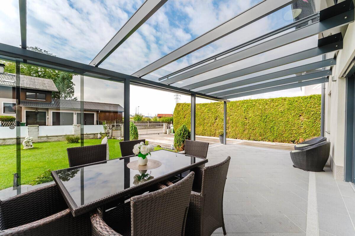 Geräumige überdachte Terrasse mit Gartenmöbeln und Blick auf die grüne Hecke.