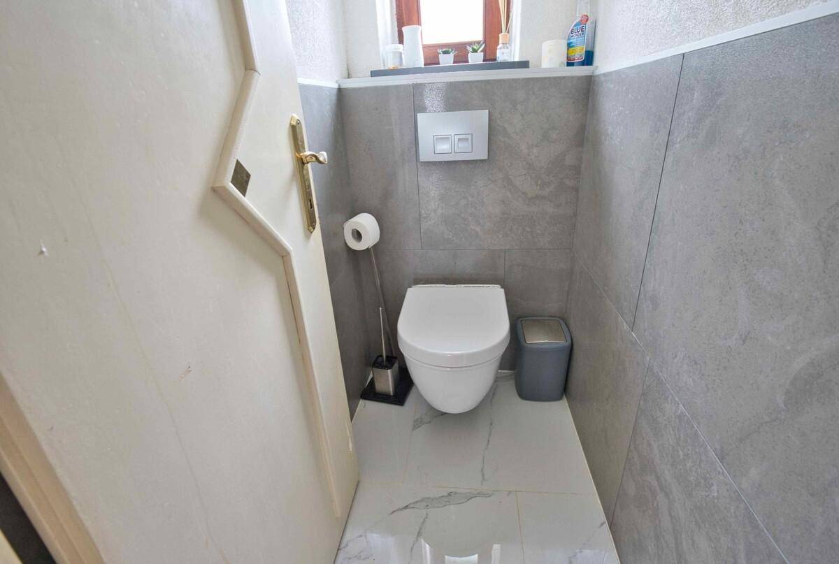 Separate Toilette mit modernen grauen Fliesen und wandhängendem WC, stilvoll und funktional.