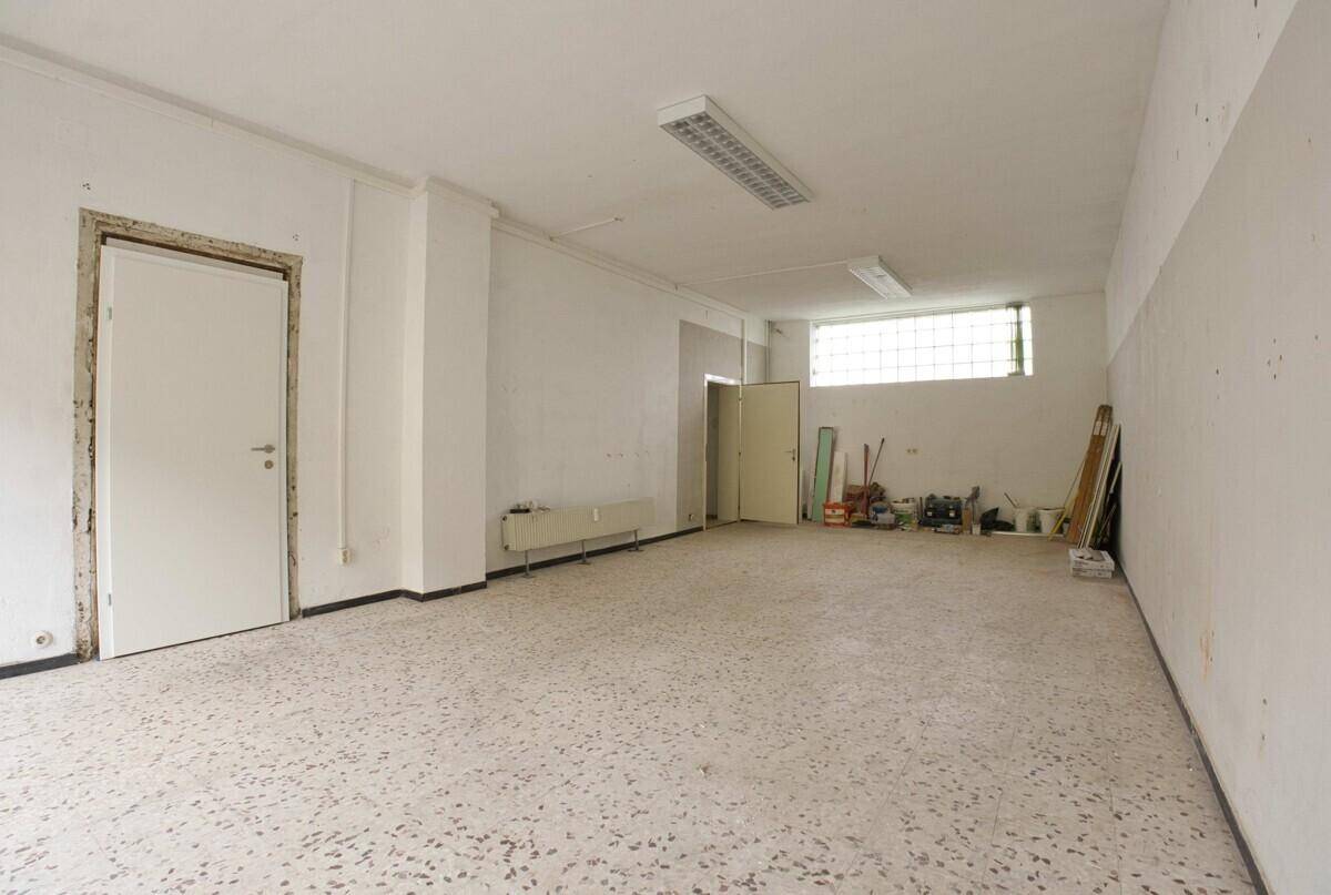 Großer, leerer Raum mit Fliesenboden und Fenstern, geeignet für gewerbliche Nutzung oder Lager.