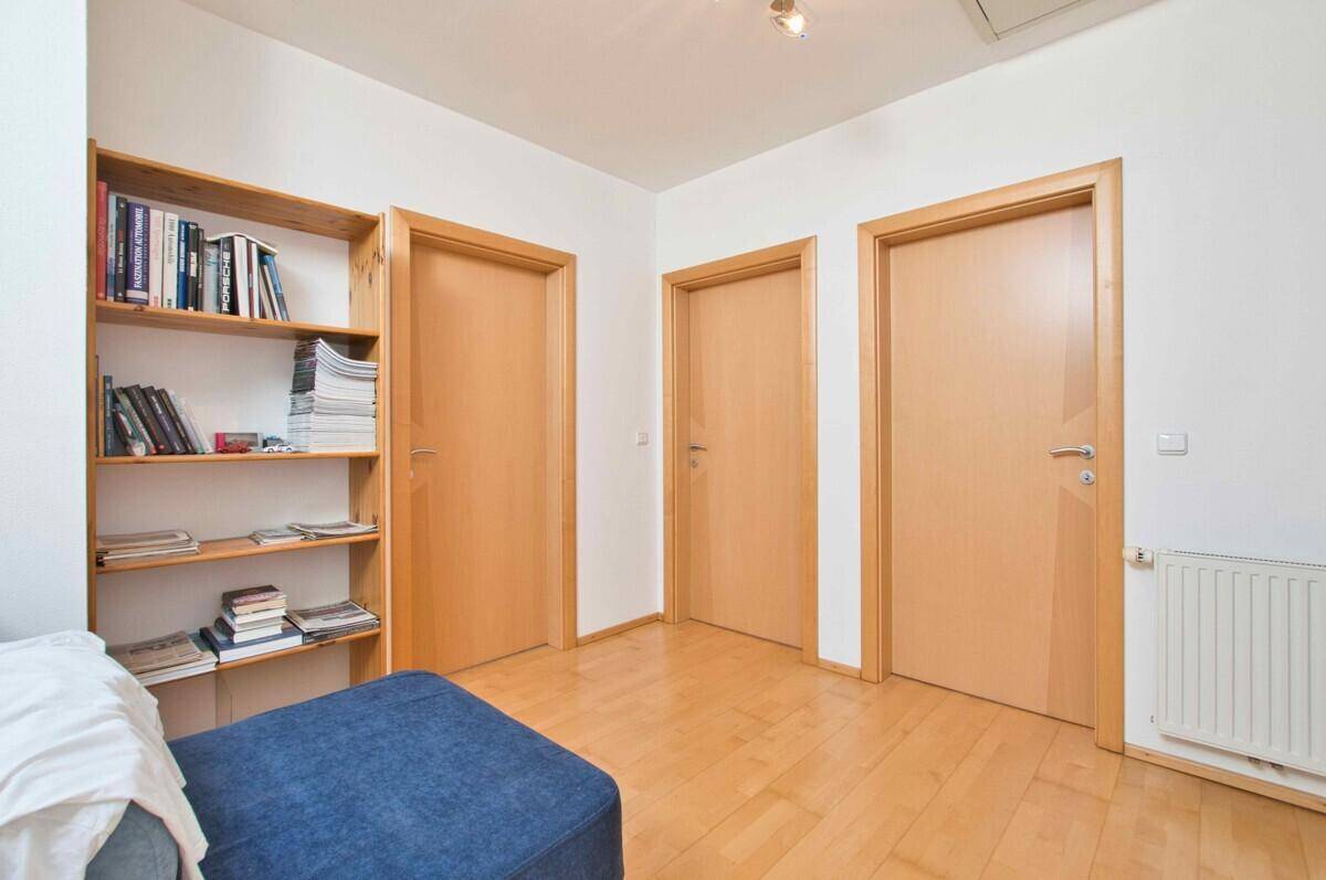 Heller Flurbereich mit Holzboden, drei Holztüren und einem Bücherregal.
