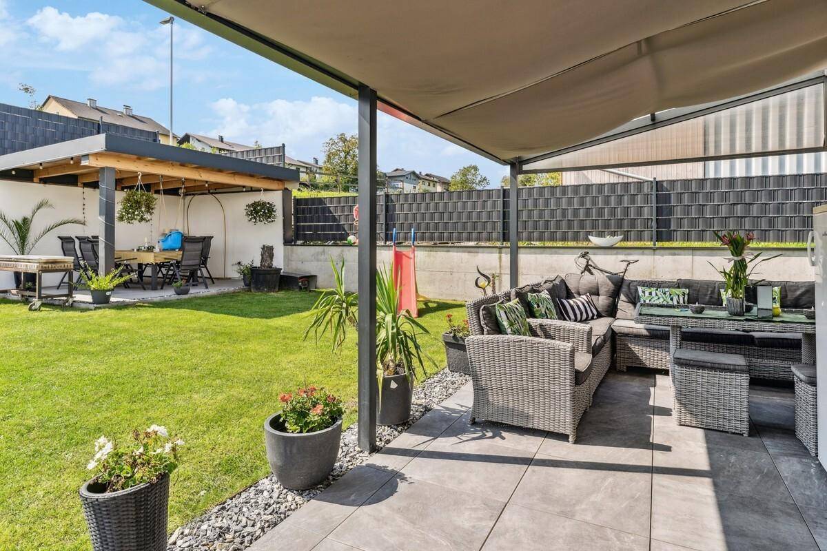 Große überdachte Terrasse mit Lounge-Möbeln und Blick in den Garten.