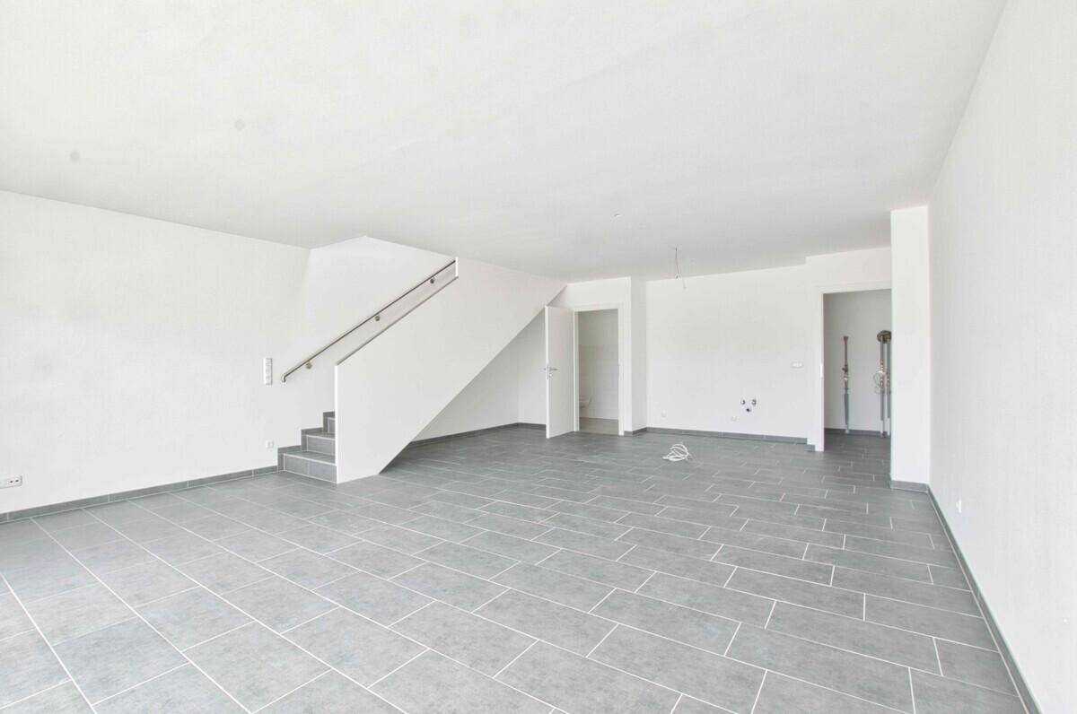 Heller, leerer Raum mit grauen Fliesen und einer modernen Treppe.