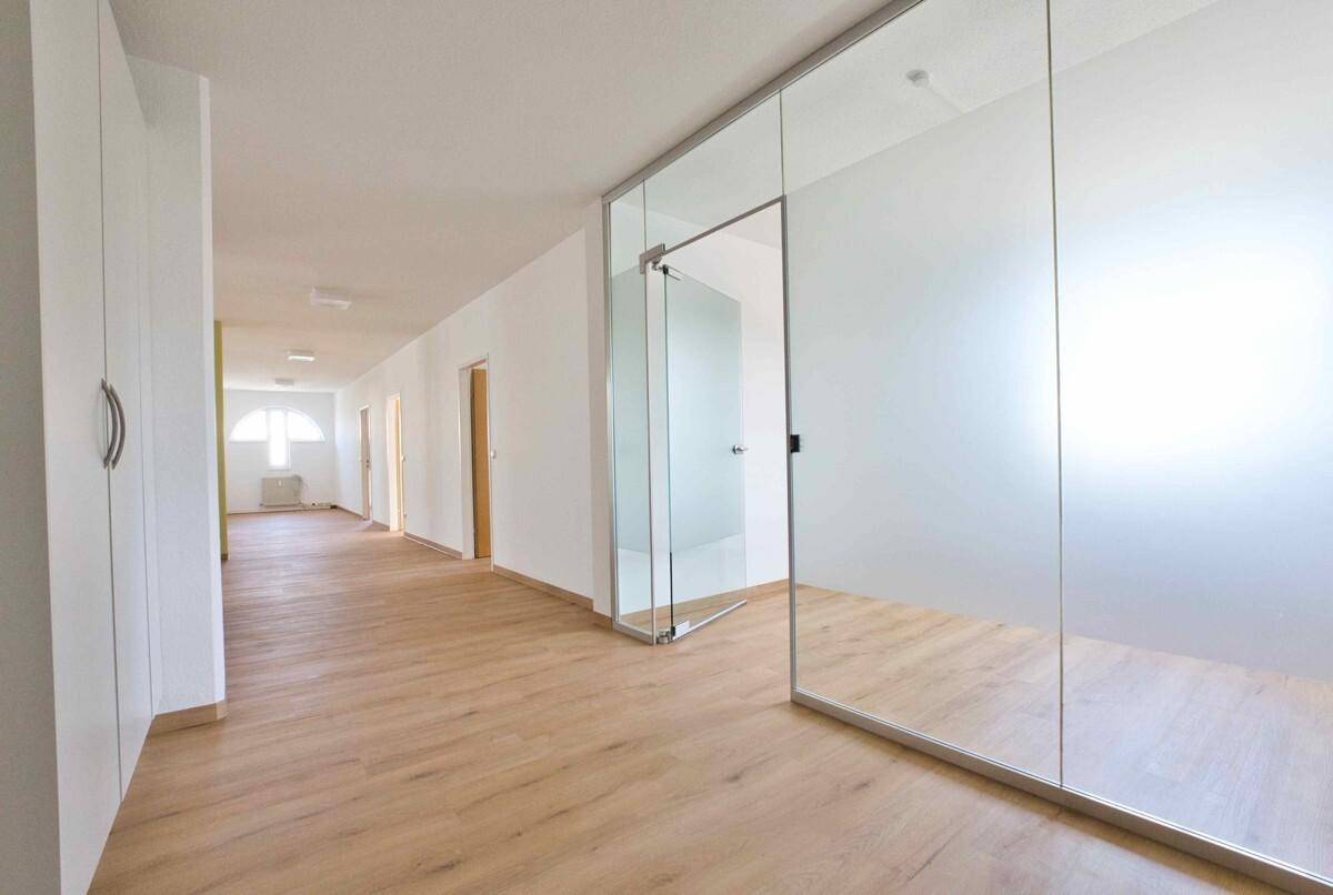 Moderner Flur mit Laminatboden, weißen Wänden und einer eleganten Glaswand zu einem angrenzenden Raum.