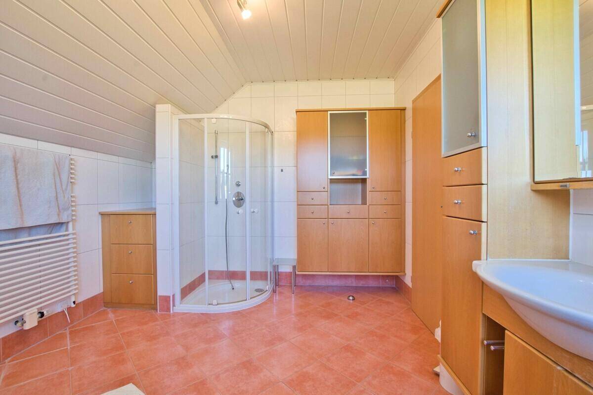 Badezimmer mit Eckdusche, Einzelwaschbecken und Holzschränken unter der Dachschräge.