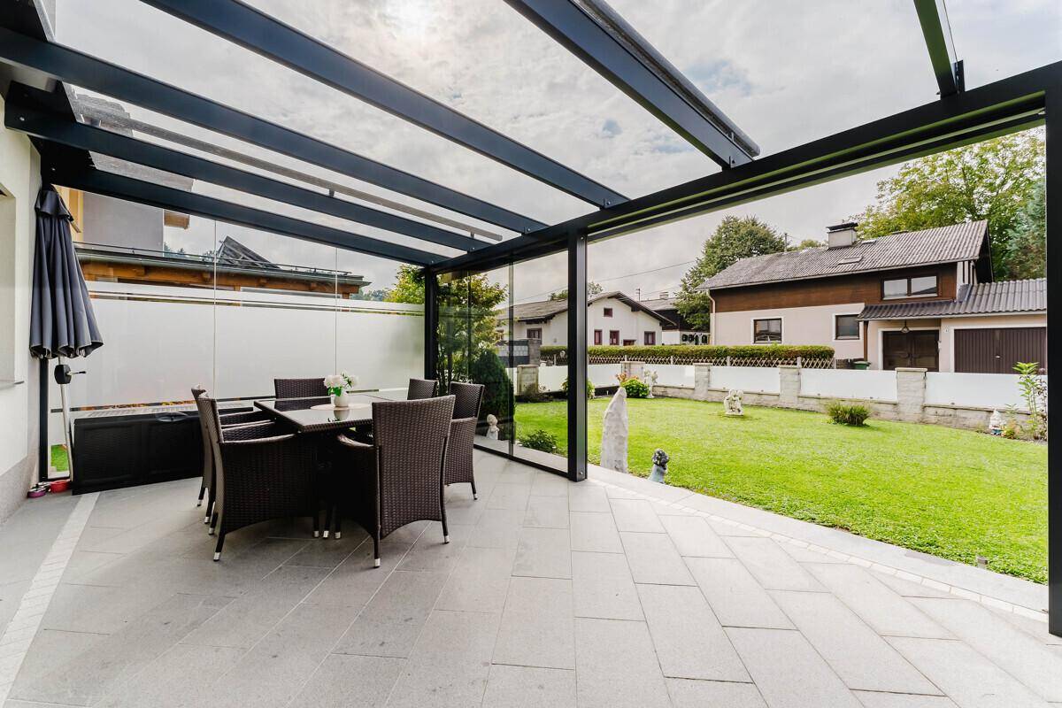 Überdachte Terrasse mit Esstisch und Stühlen, umgeben von einem gepflegten Garten.