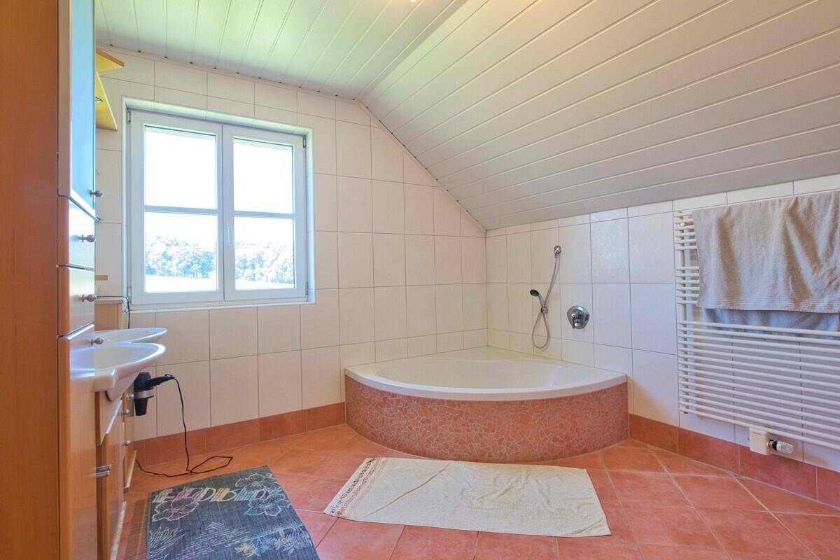 Geräumiges Badezimmer mit Eckbadewanne, Doppelwaschbecken und Terrakottaboden unter Dachschräge.