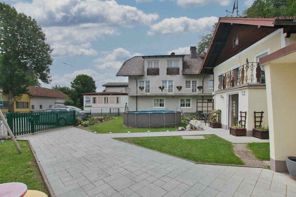 Gartenbereich mit oberirdischem Pool, Rasenfläche und gepflasterter Zufahrt.