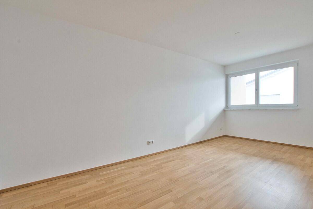 Helles, leeres Zimmer mit Holzboden und großem Fenster, bereit zur individuellen Gestaltung.