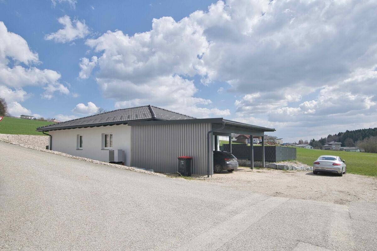 Einfamilienhaus mit modernem Carport und Zufahrt, eingebettet in ländliche Umgebung.