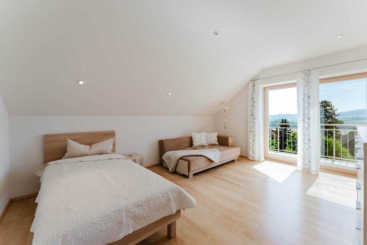 Gemütliches Schlafzimmer im Dachgeschoss mit Holzboden, Balkonzugang und schöner Aussicht.