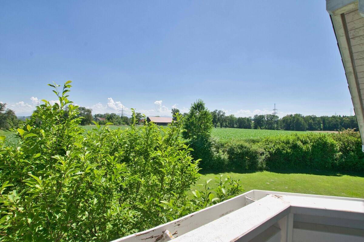 Weitläufiger Blick vom Balkon auf grüne Felder und Bäume unter blauem Himmel.