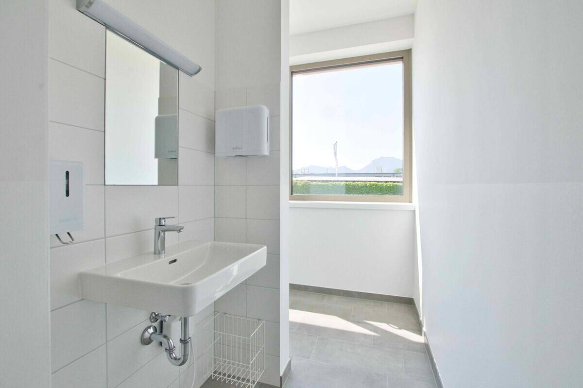 Modernes WC mit Waschbecken, Spiegel und Fenster, hell und funktional gestaltet.