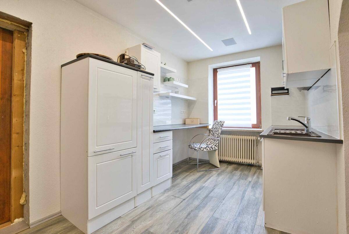 Funktionale Küche mit weißen Schränken, integriertem Kühlschrank und Vinylboden.