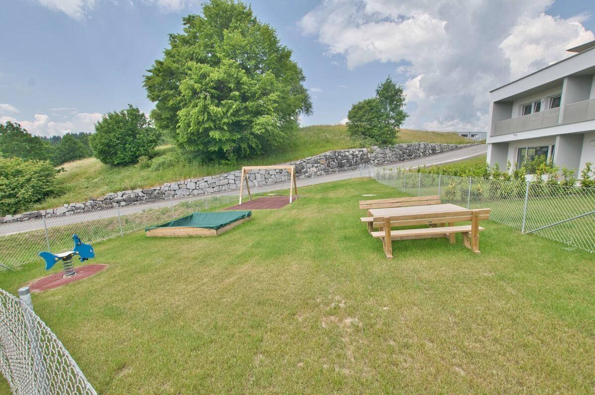 Detailansicht des Spielplatzes mit Schaukel, Sandkasten und Picknicktisch.