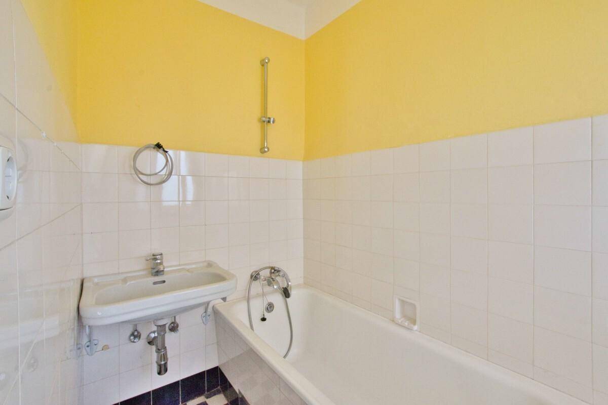 Badezimmer mit weiß gefliesten Wänden, gelber Wandfarbe, Badewanne und Waschbecken.