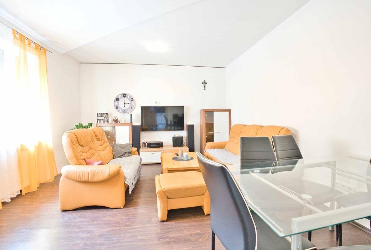 Helles Wohn-Esszimmer mit Parkettboden, beigen Sofas und einem Glastisch, ideal für gesellige Abende.