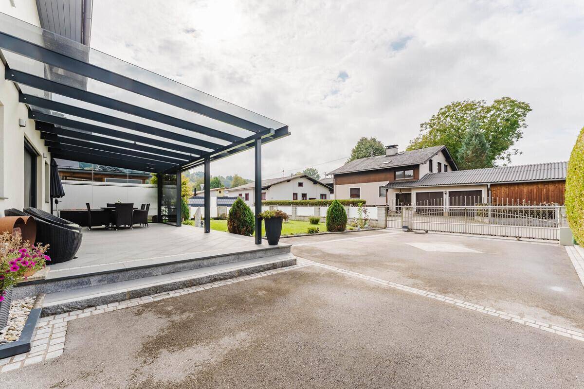 Außenbereich des Hauses mit überdachter Terrasse, Zufahrt und Blick auf die Umgebung.