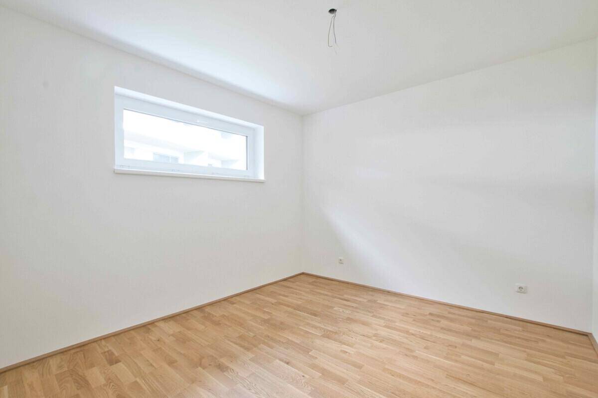 Unmöbliertes Schlafzimmer mit Holzparkettboden und einem breiten Fenster.