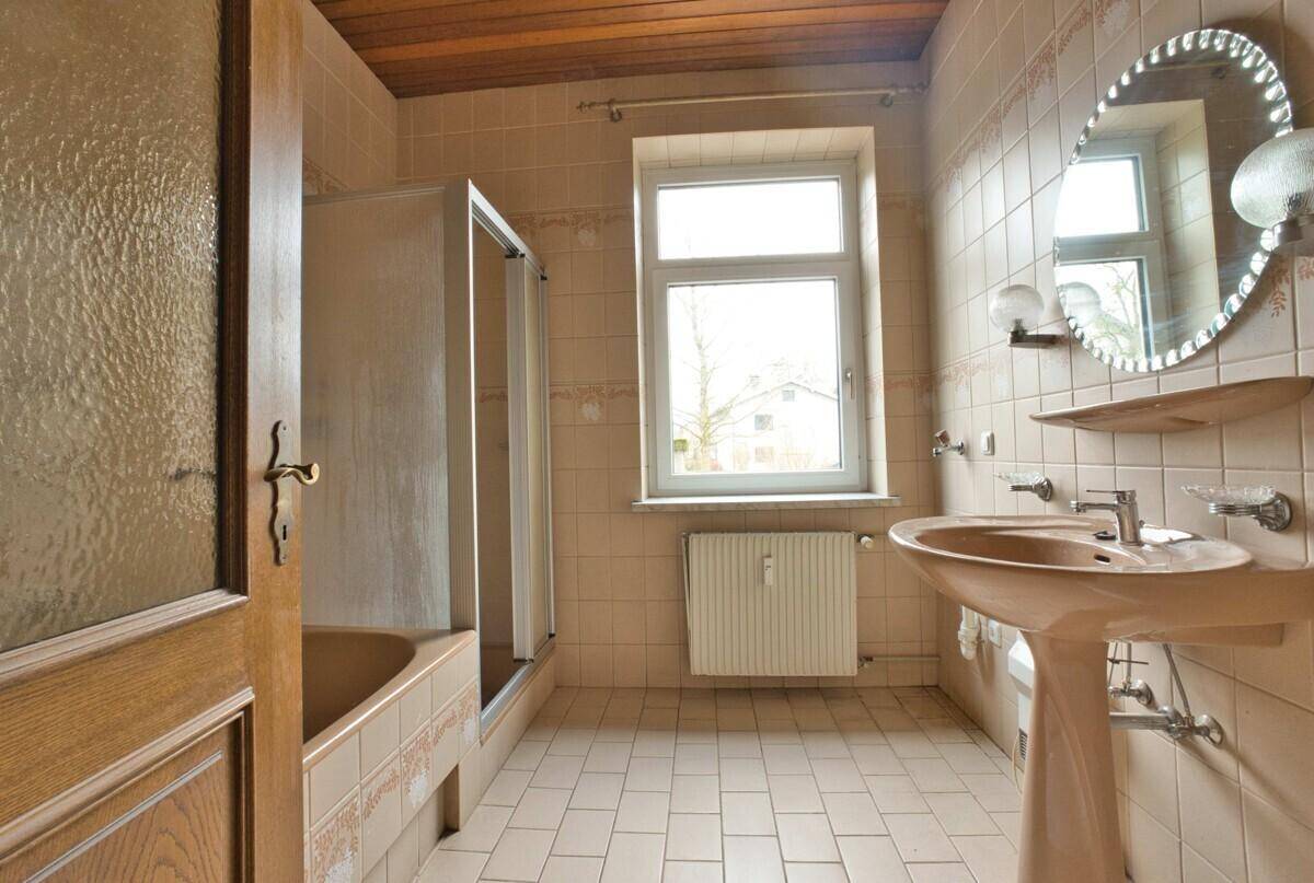 Badezimmer im 80er-Jahre-Stil mit beigefarbenen Fliesen, Badewanne und Fenster.