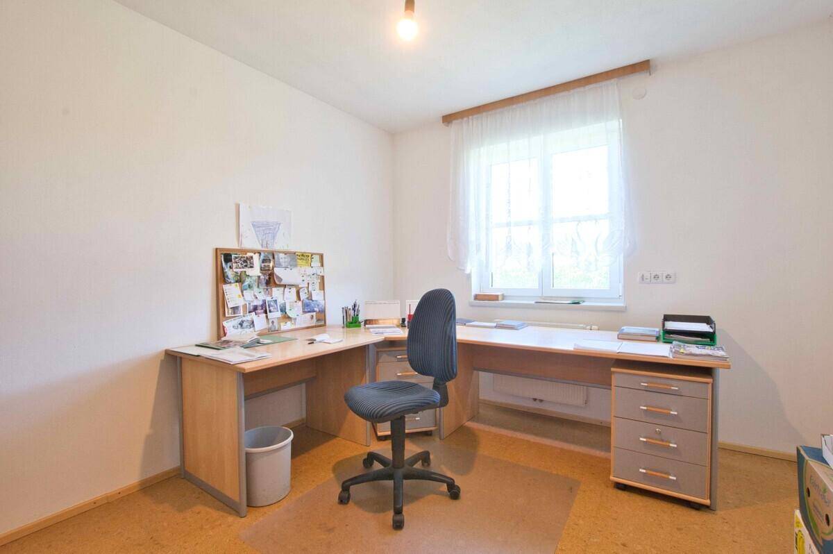 Funktionales Arbeitszimmer mit großem Schreibtisch, Bürostuhl und Fenster mit Blick ins Grüne.