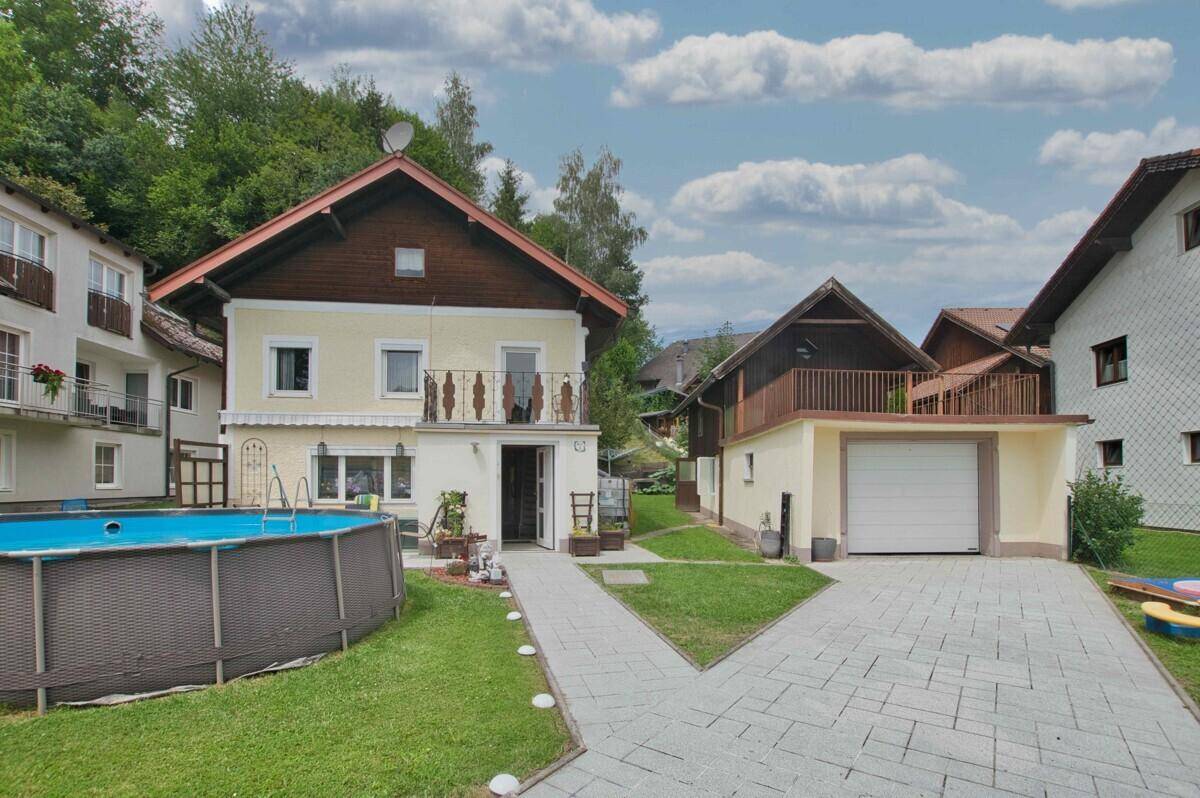 Hausansicht mit Garage, Garten, oberirdischem Pool und gepflasterter Einfahrt.