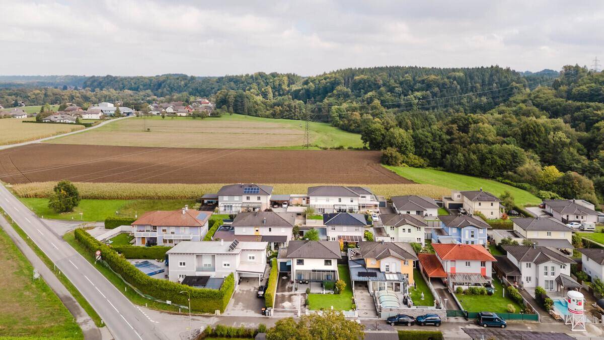 Luftaufnahme einer Wohnsiedlung umgeben von Feldern und Wäldern in ländlicher Umgebung.