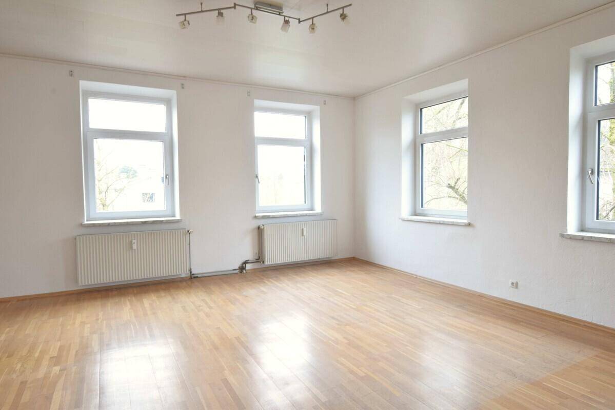 Geräumiges, helles Wohnzimmer mit Laminatboden und mehreren Fenstern, ideal für Familien.