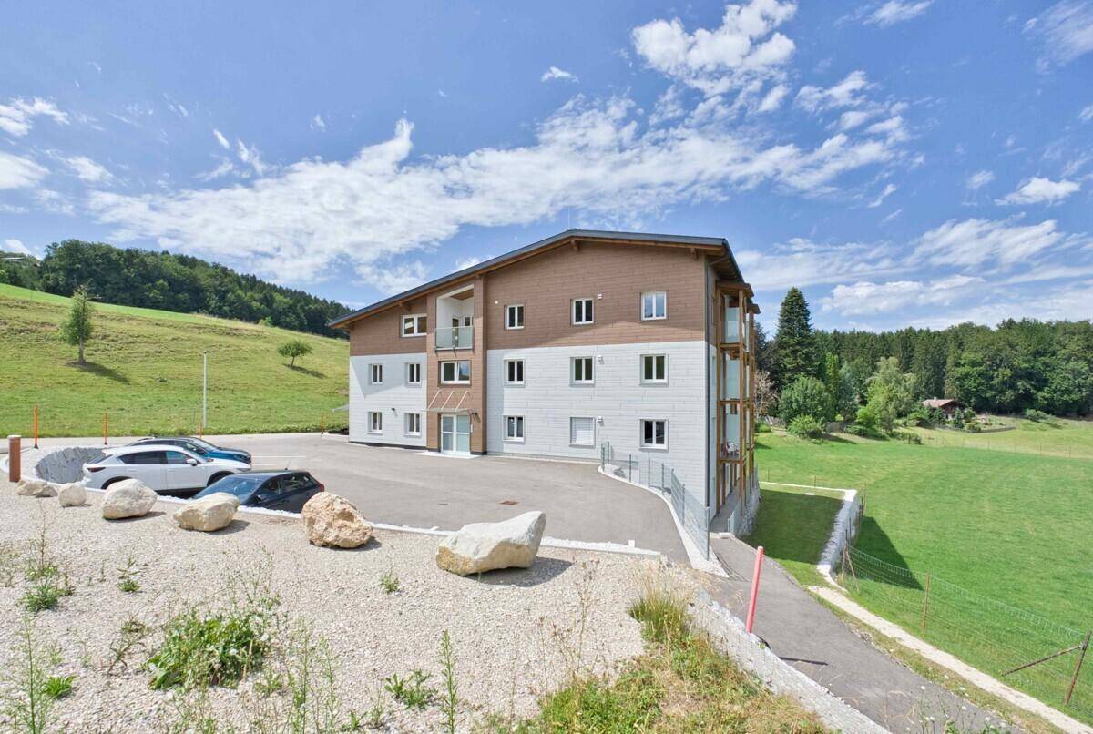 Neues Wohngebäude mit moderner Fassade, Parkplätzen und Zufahrt in ländlicher Umgebung.
