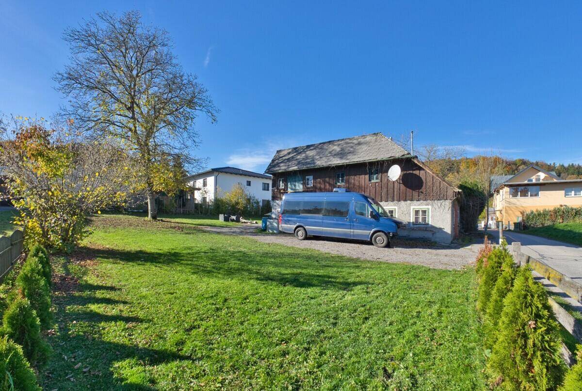 Außenansicht des Hauses mit großem Rasen, altem Baumbestand und blauem Himmel an einem sonnigen Tag.