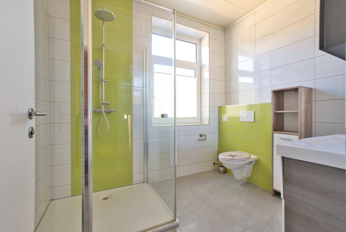 Modernes Badezimmer mit grünen Akzentfliesen, Dusche, WC und Fenster.