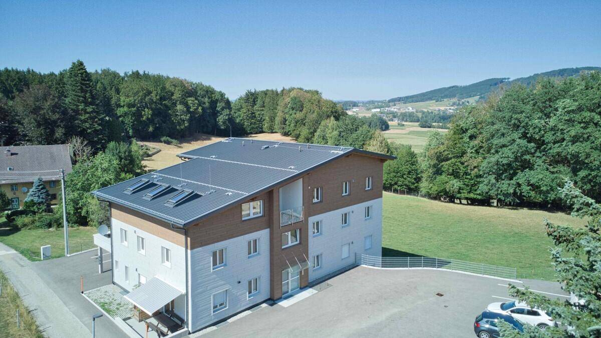 Luftaufnahme eines modernen Mehrfamilienhauses mit Satteldach und umliegender grüner Landschaft.