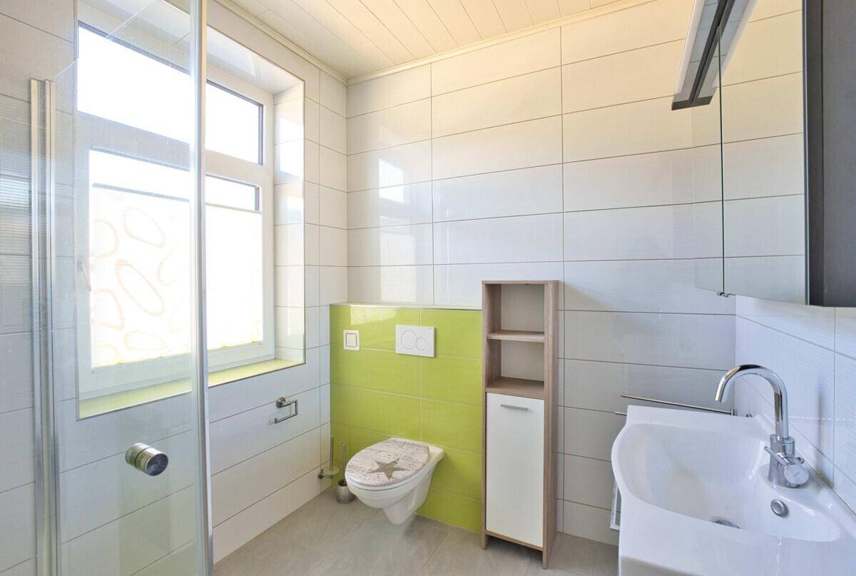 Modernes Badezimmer mit grünen Akzentfliesen, Dusche, WC und Waschtisch mit Spiegelschrank.