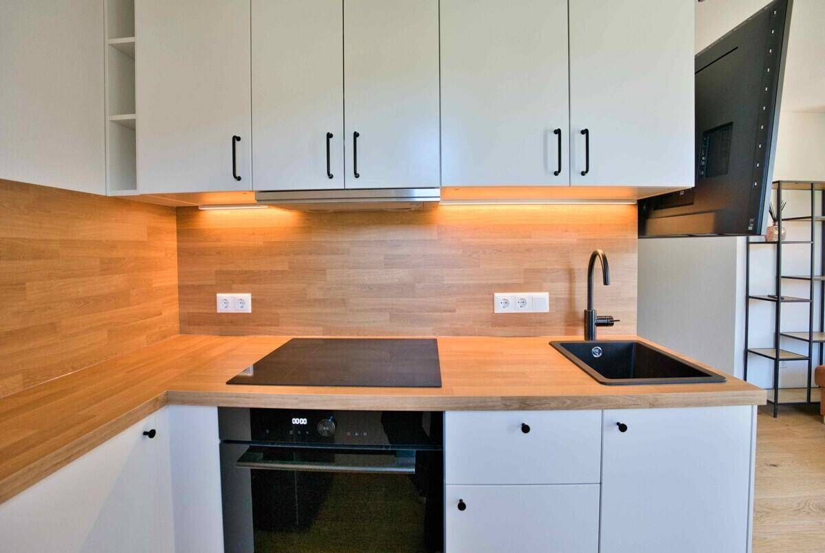 Moderne Küche mit weißen Schränken, Holz-Arbeitsplatte und integrierten Geräten. Die Küche verfügt über eine Induktionskochplatte und einen Backofen.