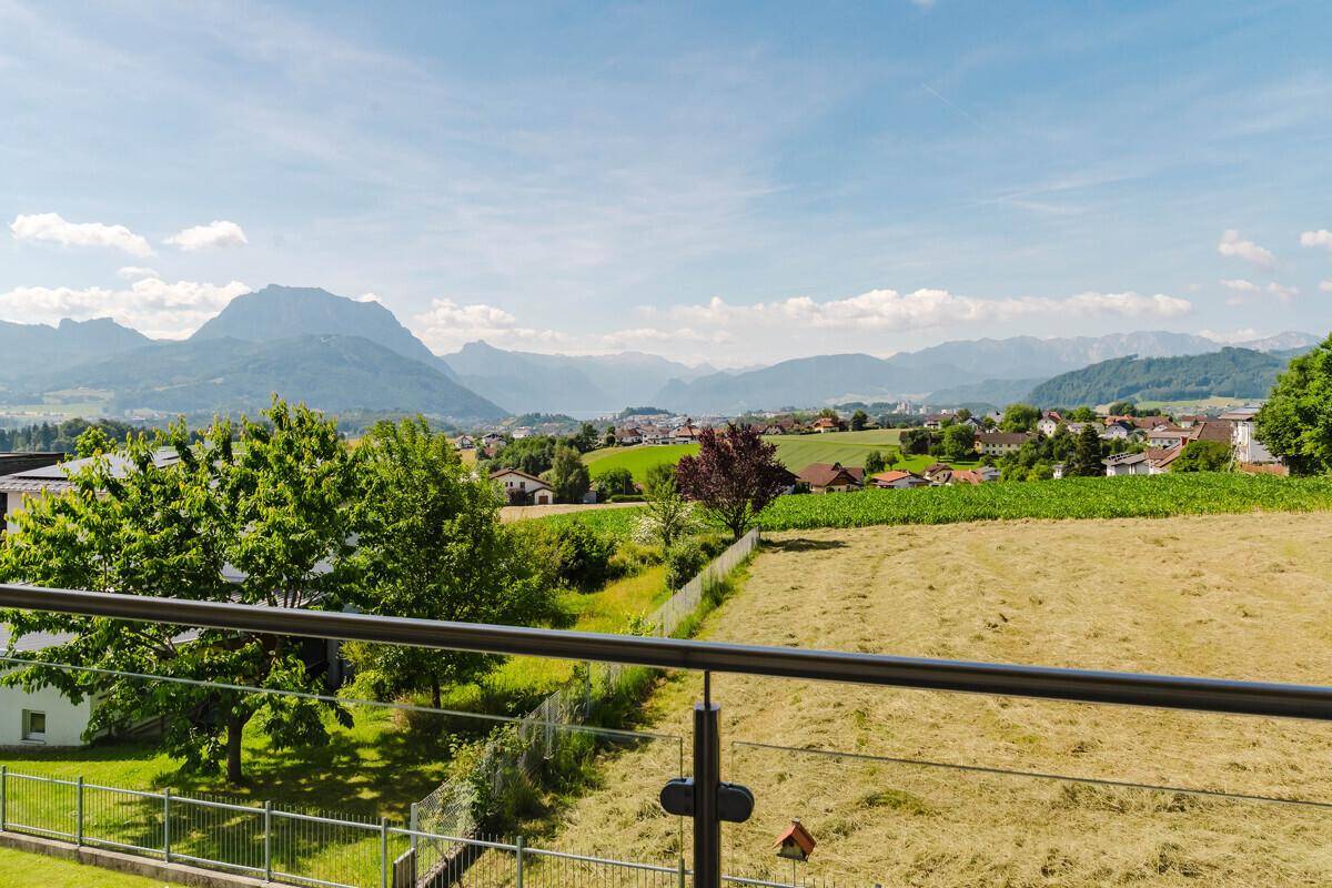 Weitläufiger Ausblick vom Balkon über grüne Felder und die majestätische Berglandschaft.
