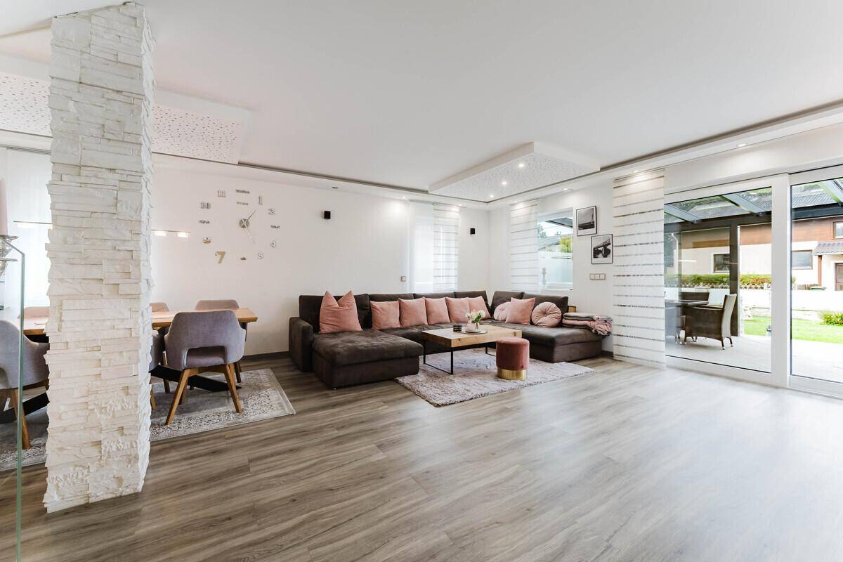Lichtdurchfluteter Wohn-Essbereich mit großem Sofa, Esstisch und Zugang zur Terrasse.