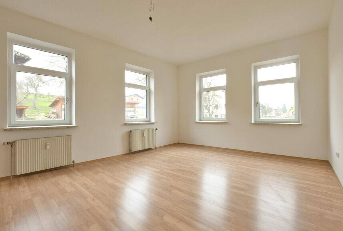 Helles, leeres Zimmer mit Laminatboden und mehreren Fenstern, ideal für Wohn- oder Schlafbereich.