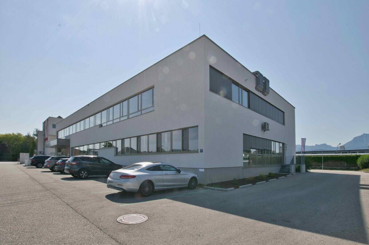 Modernes Bürogebäude mit Parkplätzen unter blauem Himmel, in gepflegter Umgebung.