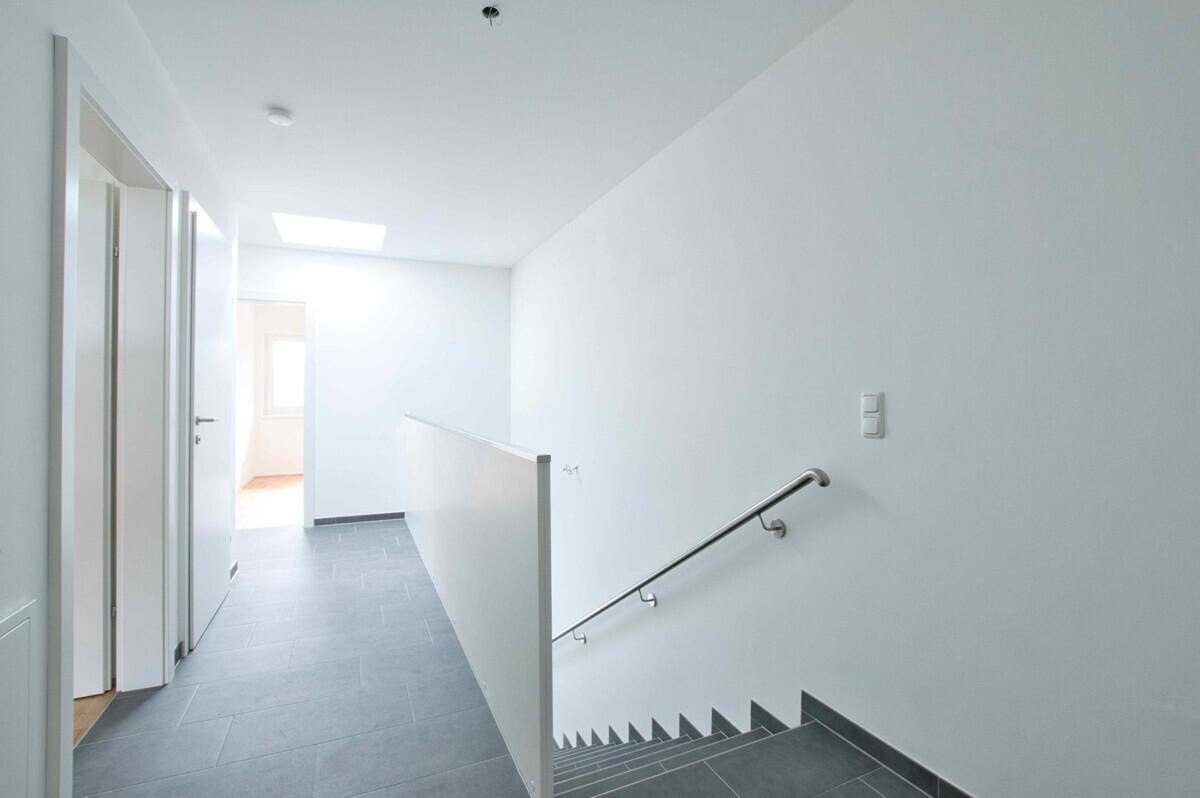 Heller Flur mit Fliesenboden, Treppe und einem Oberlicht für natürliches Licht.