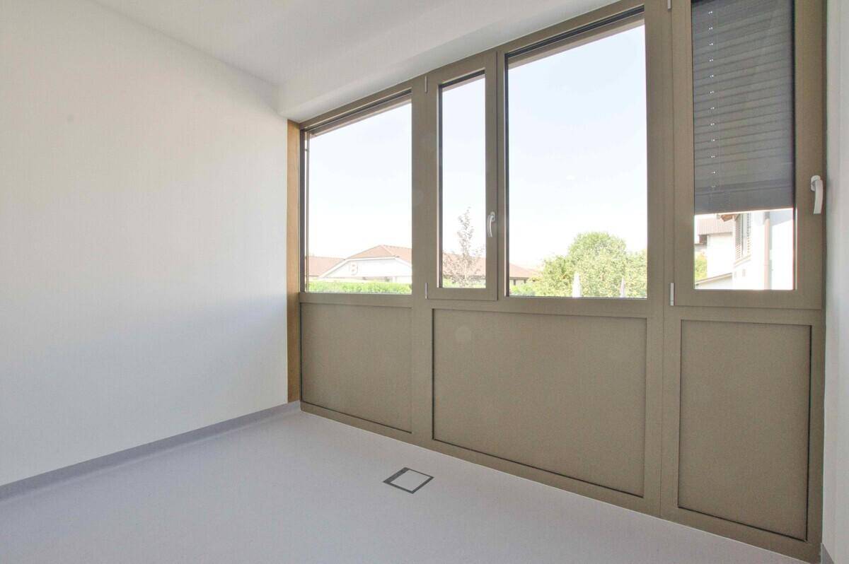 Heller Raum mit breiter Fensterfront und Rollladen, bietet viel Tageslicht und Privatsphäre.