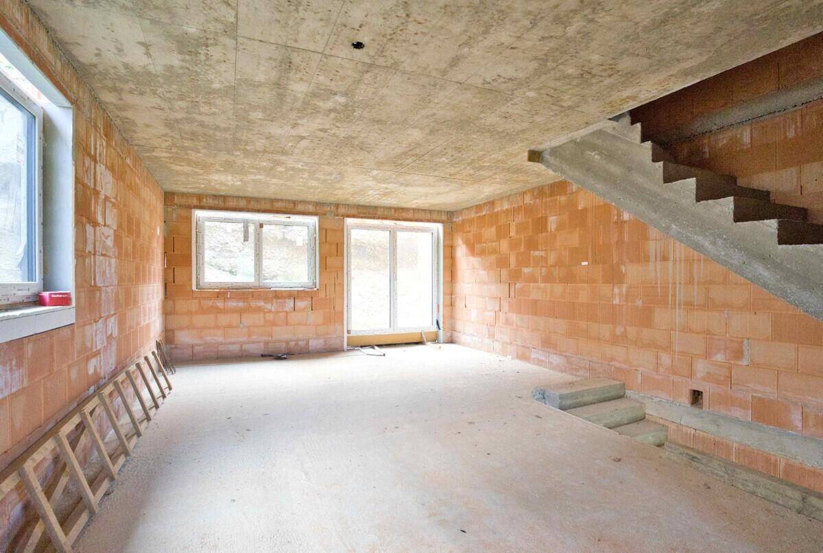 Geräumiger Innenraum im Rohbau mit Betonboden, Ziegelwänden und großen Fensteröffnungen für viel Licht.