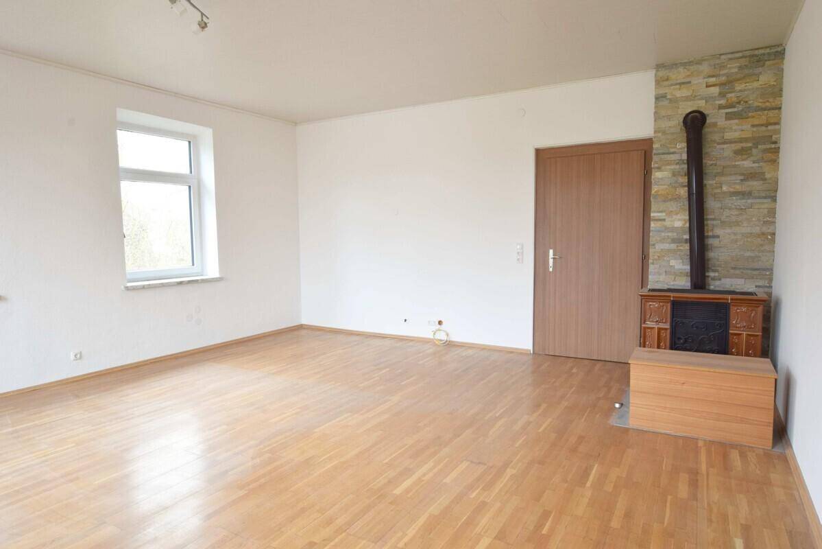 Helles Zimmer mit Laminatboden und Kaminofen mit Steinverkleidung, ideal für gemütliche Abende.