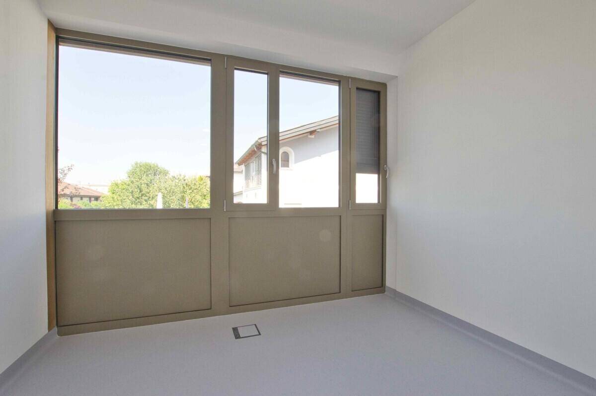 Leerer Raum mit großer Fensterfront und Blick ins Grüne, ideal für Büro oder Praxis.