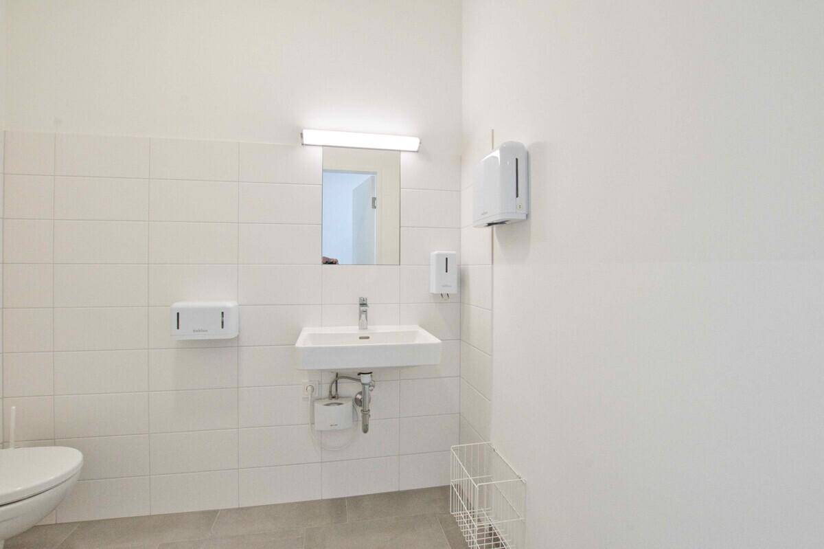 Funktionales WC mit Waschbecken, Spiegel und Toilette, in hellem Design gehalten.