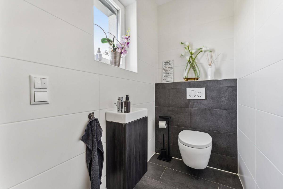 Modernes Gäste-WC mit dunklen und weißen Fliesen, wandhängendem WC und kleinem Waschbecken.