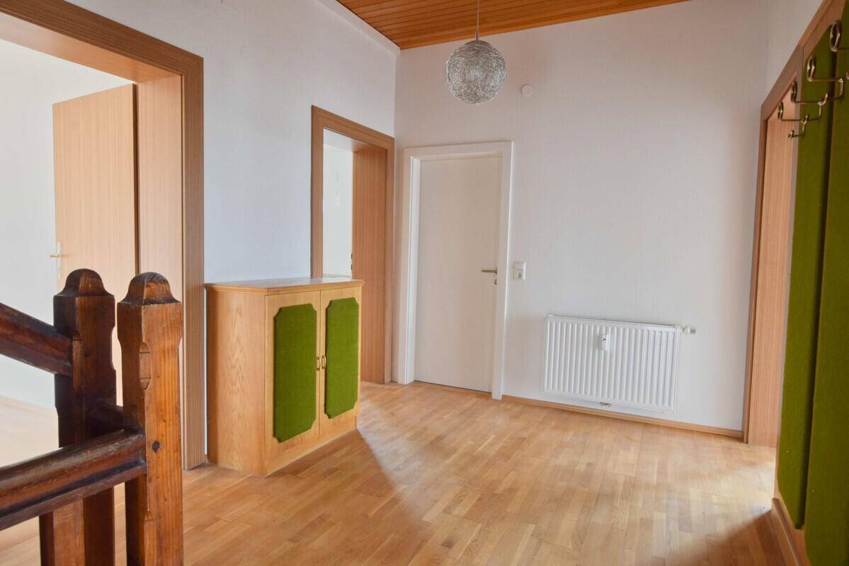 Heller Flur mit Holztreppe, Laminatboden und Garderobenbereich, der zu den oberen Etagen führt.