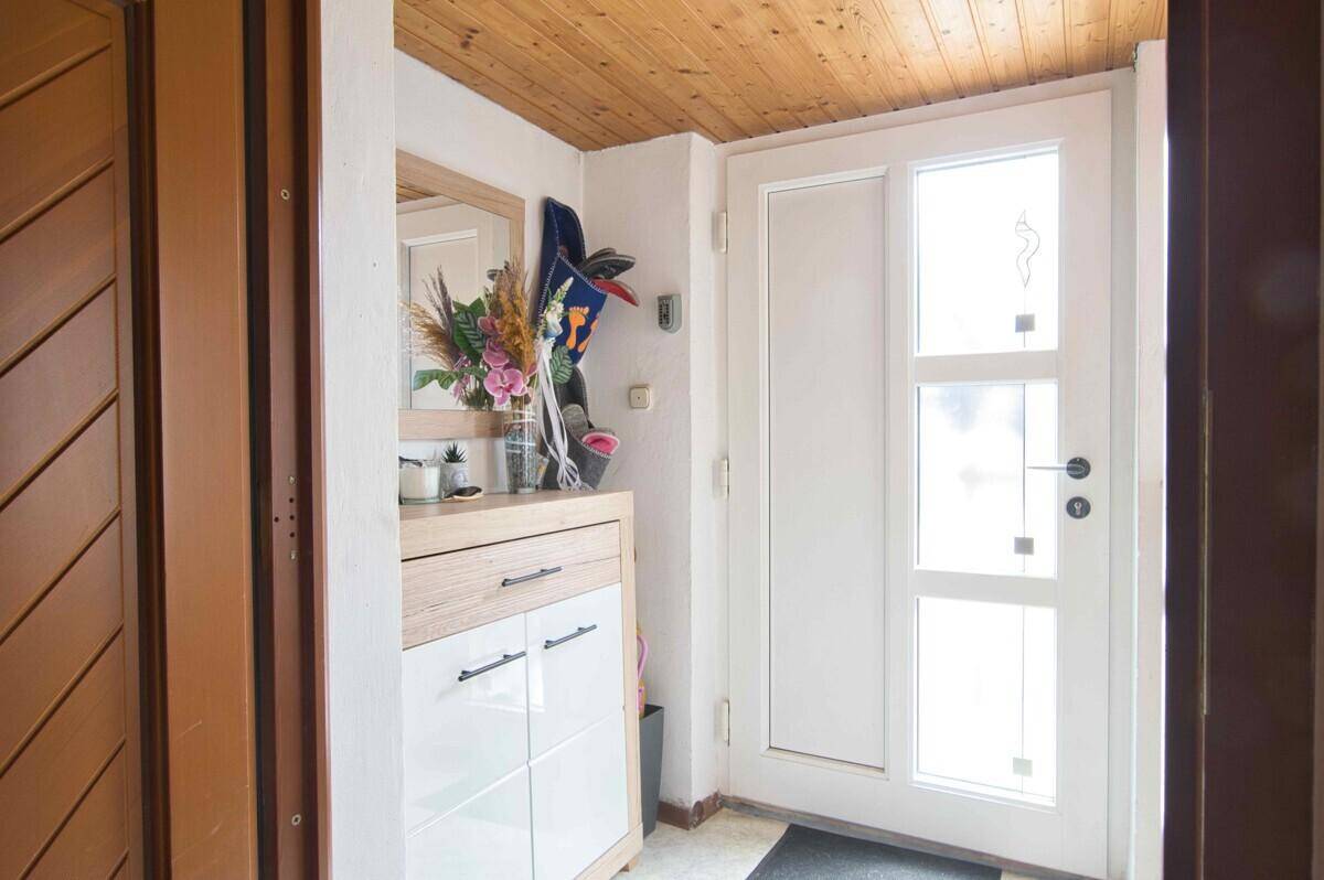 Eingangsbereich mit heller Haustür, Schuhschrank und Holzpaneeldecke.