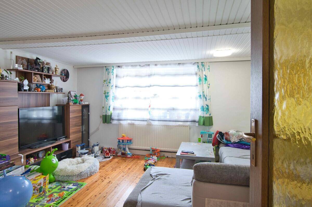 Helles Wohnzimmer mit TV-Möbeln, großem Fenster und Spielzeug auf dem Boden.